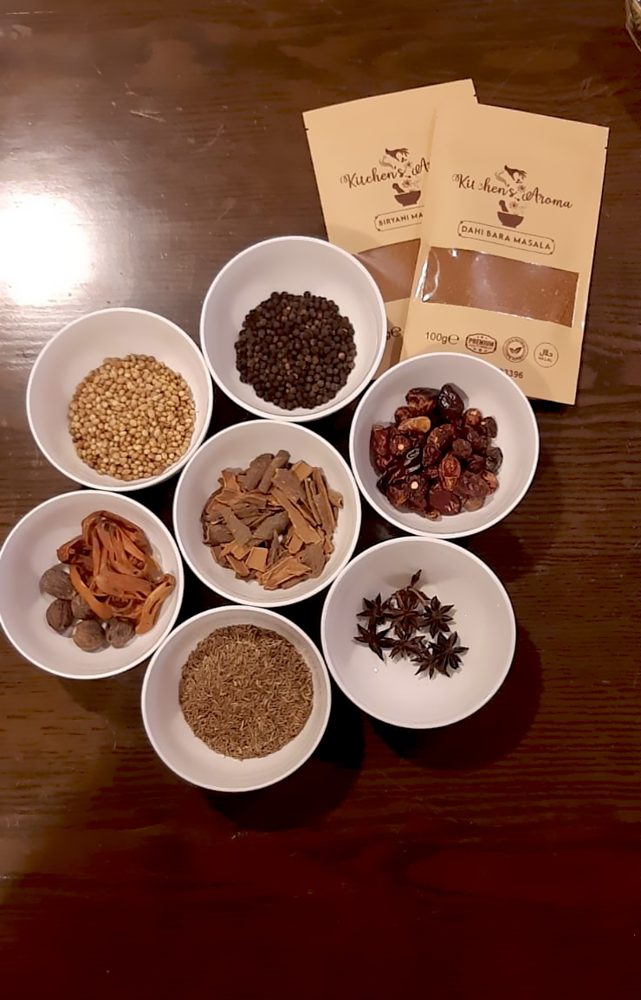 Whole spices in white bowls beside masala pouches